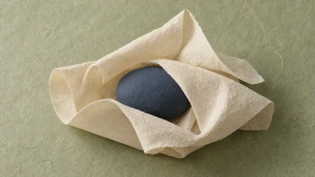 A smooth navy oval nestled in folds of textured cream paper on a pale green background.