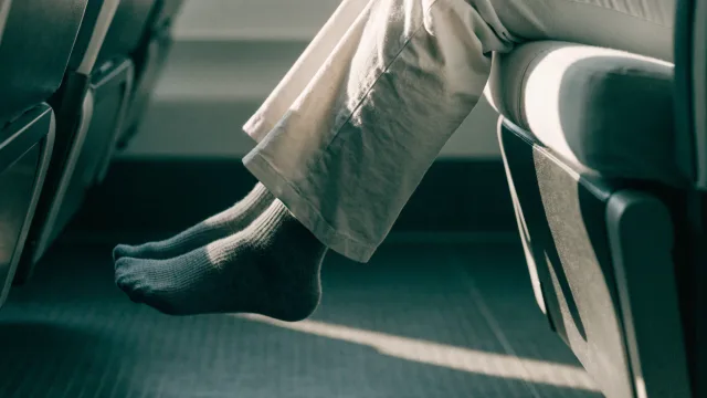 Exactly one postoperative passenger performing gentle ankle pumps in an aisle seat, framed only from knees downward with no face