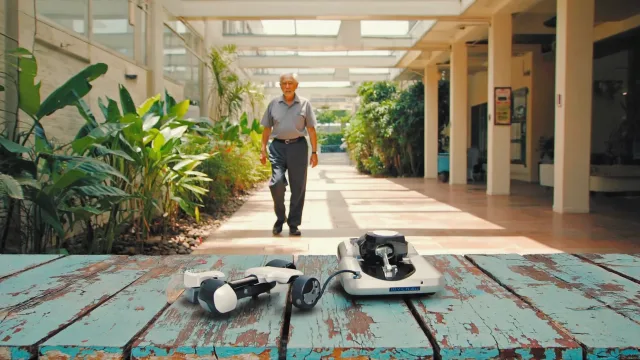 An older Indian patient walking confidently through a sunlit hospital garden, with compact robotic knee equipment in the foreground